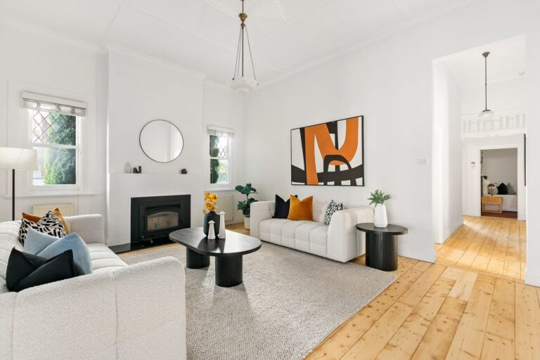 White Coburg staged lounge room, black fireplace with light timber floor. white and lack colours used with a burst of orange themed art and cushions.