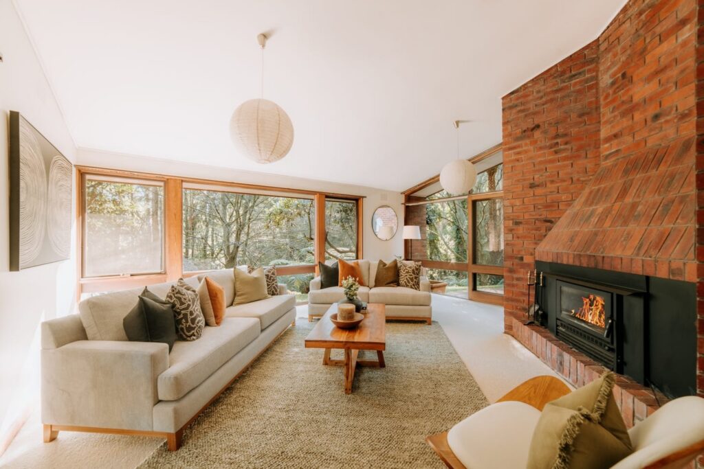 Staged living room with neutral sofas, brick fireplace and forest views in a house in Olinda
