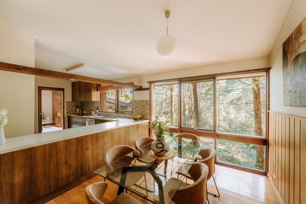 Dining area with timber cabinetry, glass dining table and woodland views in a house in Olinda