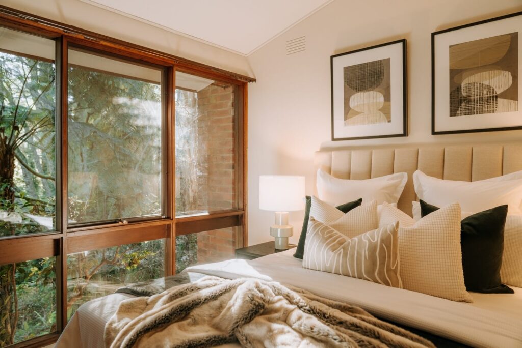 Staged bedroom with neutral bedding, green accents and floor-to-ceiling garden views in a house in Olinda