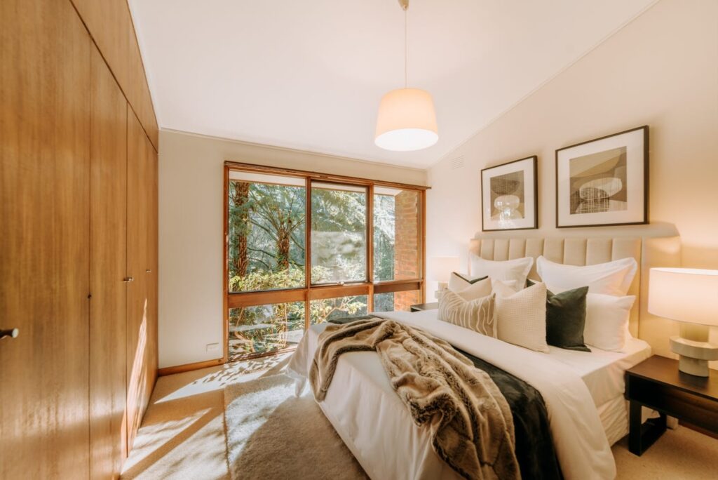 Warm neutral bedroom with layered bedding, timber wardrobes and forest views in a house in Olinda