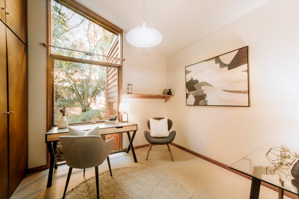 Home office with timber desk, neutral furniture and large woodland window in a house in Olinda