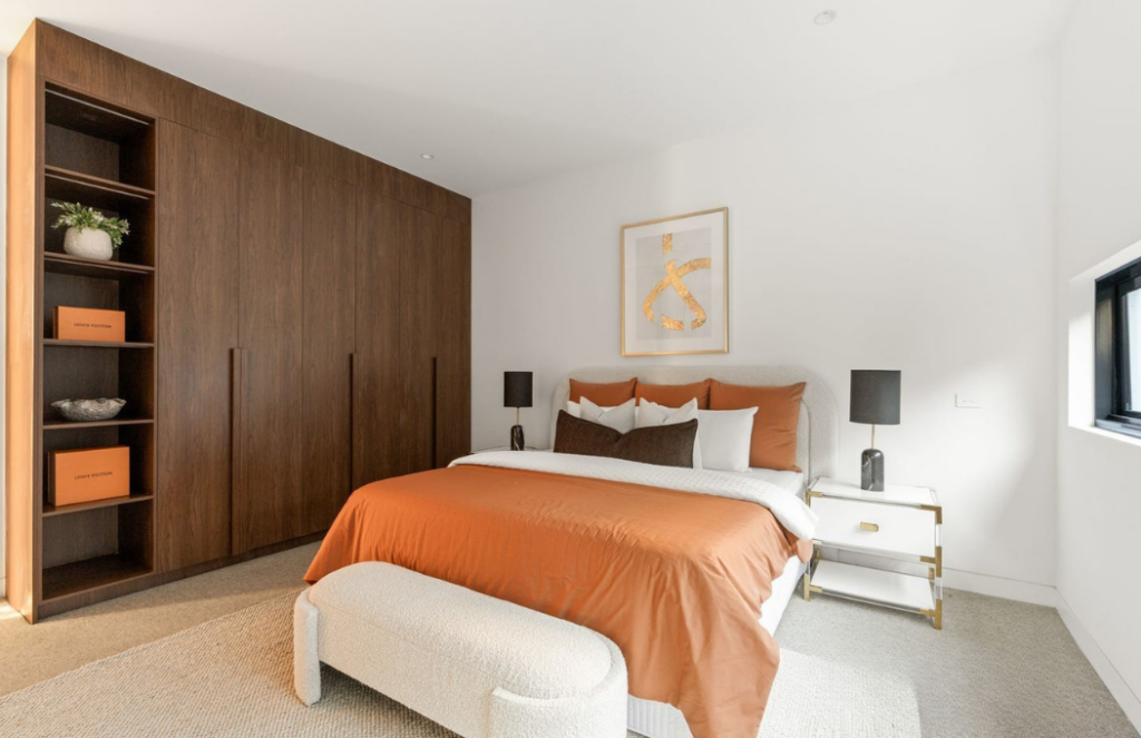 Glen Iris main bedroom staging. orange styled linen, king bed with gold art behind. White ottoman at the foot of the bed.