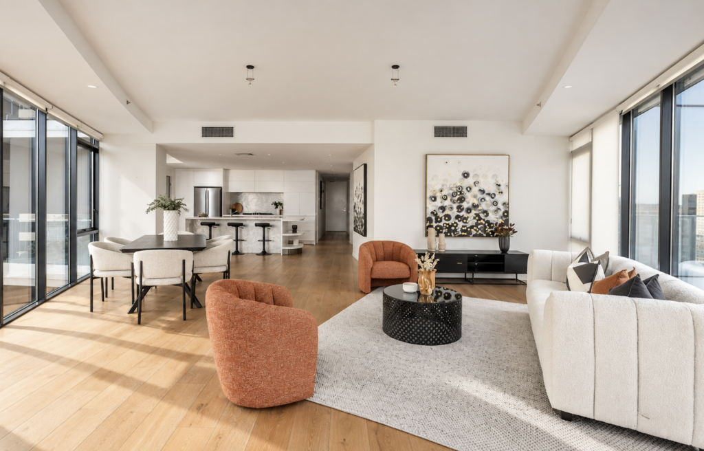 Professionally staged open-plan living and dining area with curved white sofa and rust accent chairs in an apartment in the Melbourne CBD.