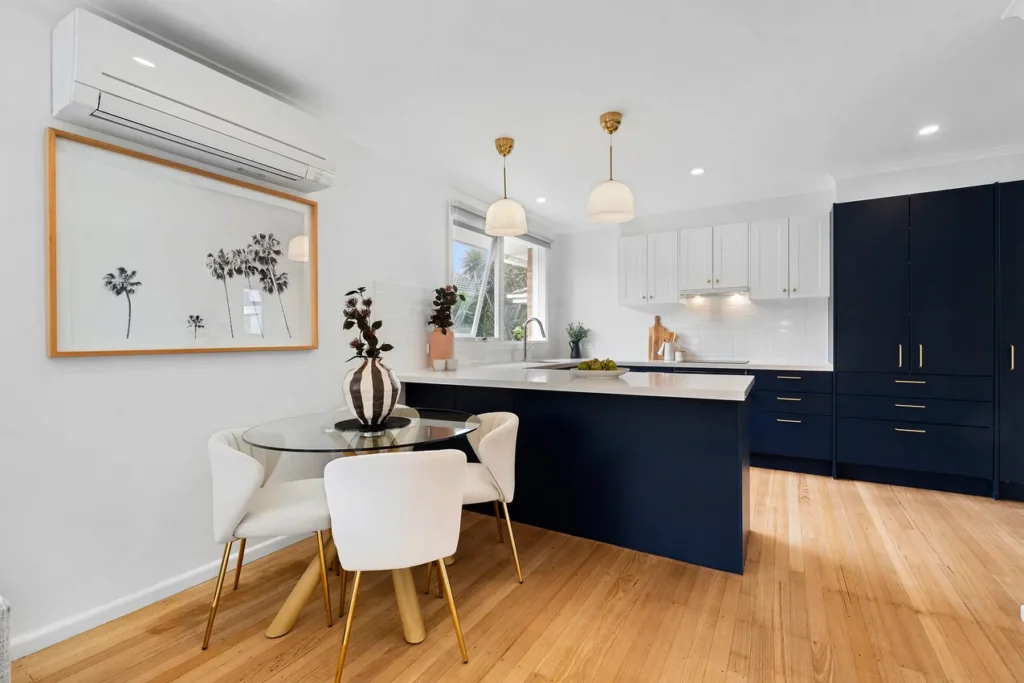 a modern staged kitchen with navy cupboards and white walls. dining and kitchen connected.