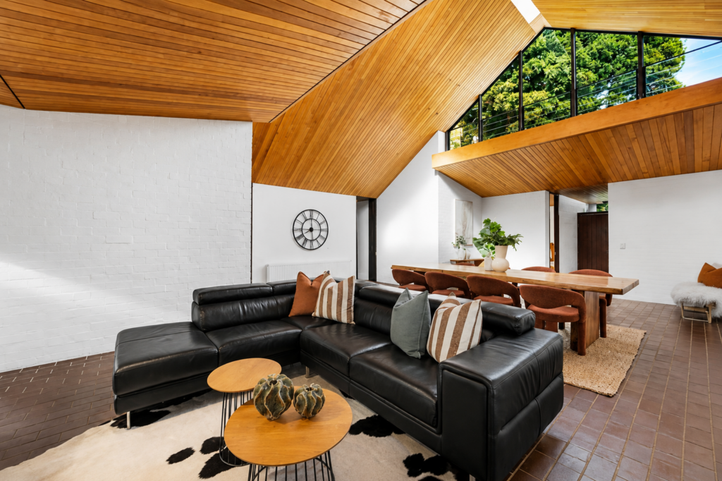 A staged family room with a cow rug under a black couch, with a tall and exponential roof.