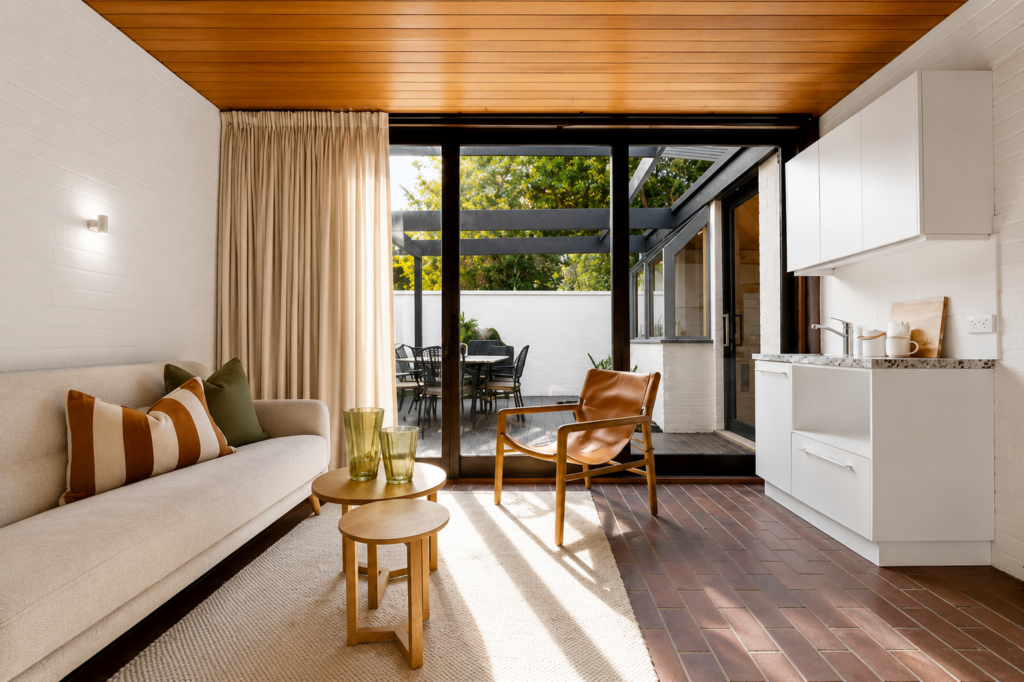 A staged rumpus room in Blackburn with a white couch, timber roof white rug, brown armchair and warm accessories.