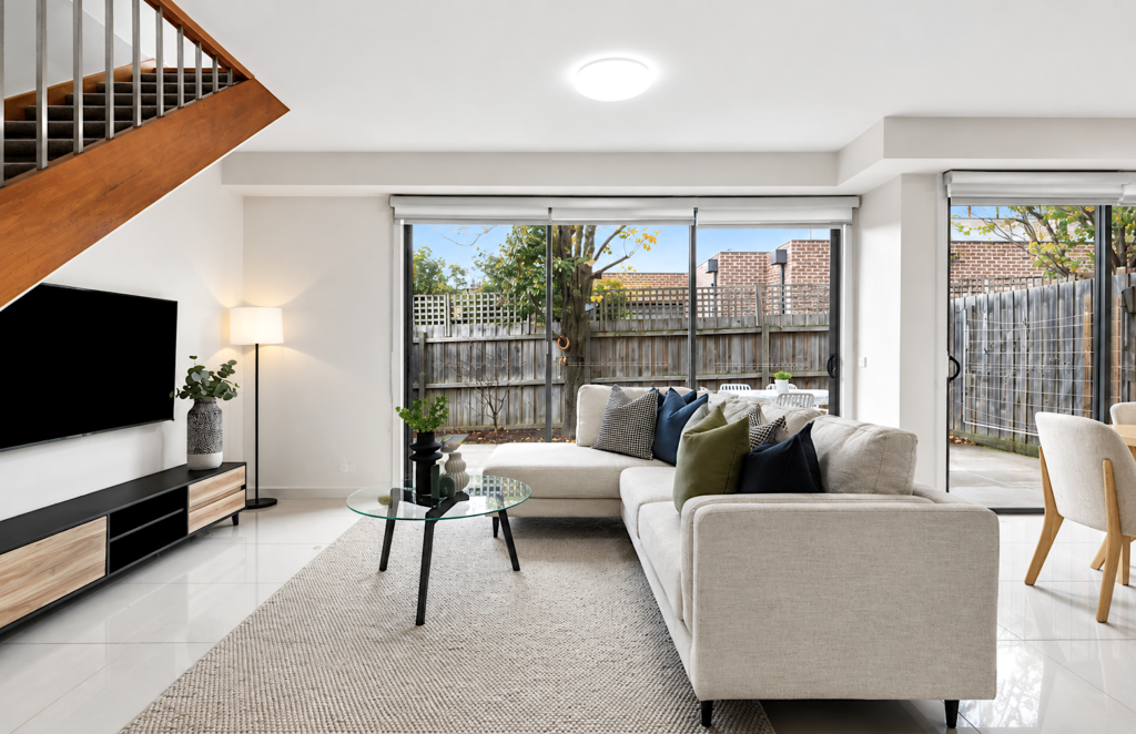 Modern staged living room with neutral sofa, glass coffee table and open-plan design in a townhouse in Carnegie.