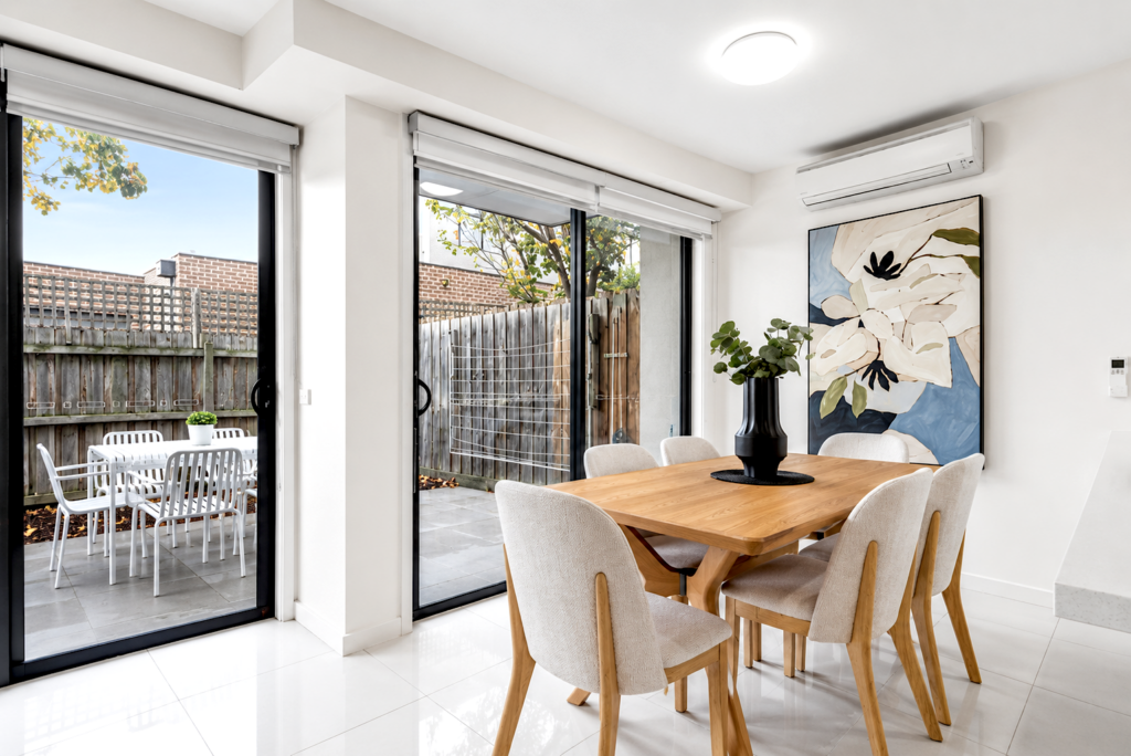 Light-filled dining area with timber dining table, contemporary artwork and garden outlook in a townhouse in Carnegie.