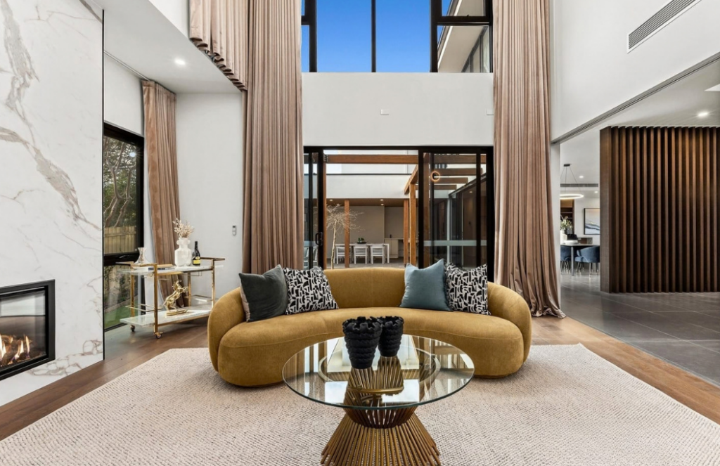 Curved mustard sofa, glass coffee table and dramatic double-height curtains in a luxury house in Doncaster.