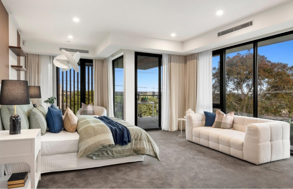 Large bedroom with green bedding, textured white sofa and expansive windows overlooking the trees in a luxury house in Doncaster.