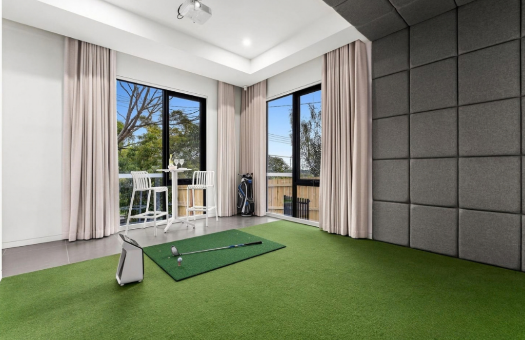 Indoor golf practice room with putting turf, golf equipment and large corner windows in a luxury house in Doncaster.