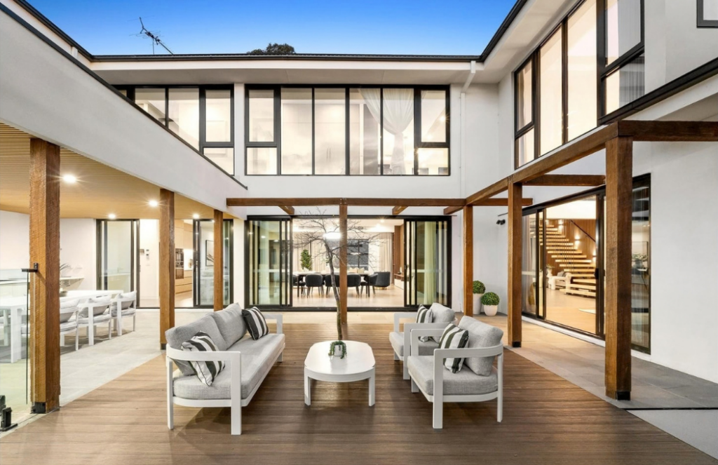 Central courtyard with outdoor lounge furniture, timber decking and surrounding floor-to-ceiling windows in a luxury house in Doncaster.