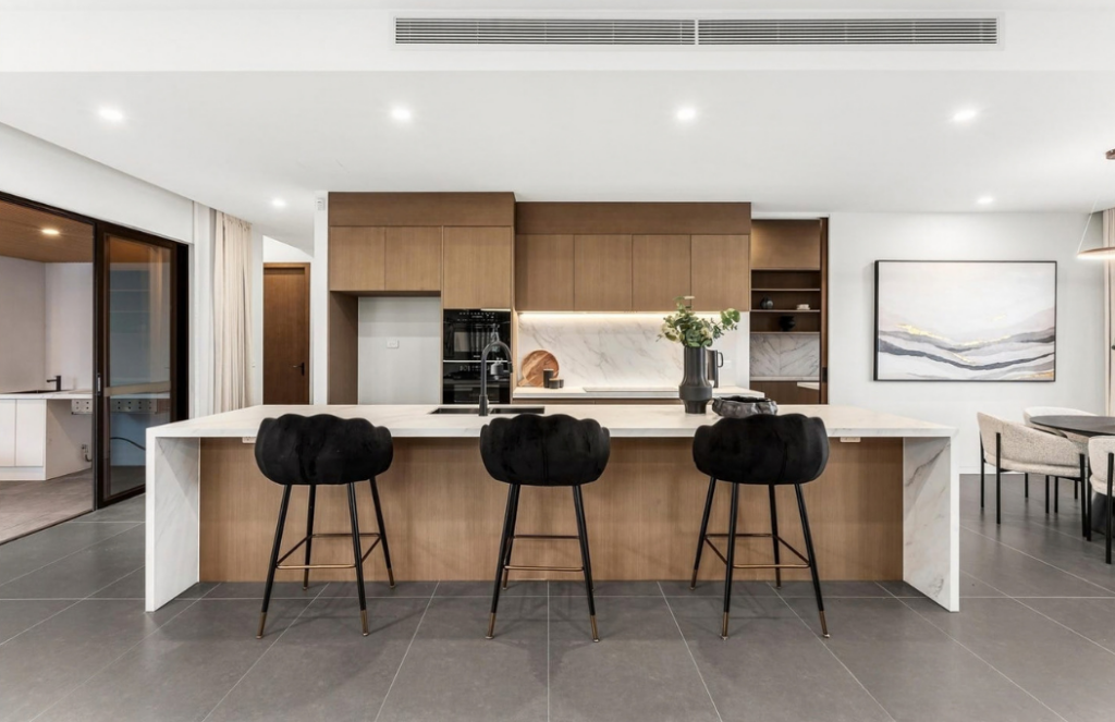 Contemporary kitchen with warm timber cabinetry, marble finishes and black bar stools in a luxury house in Doncaster.