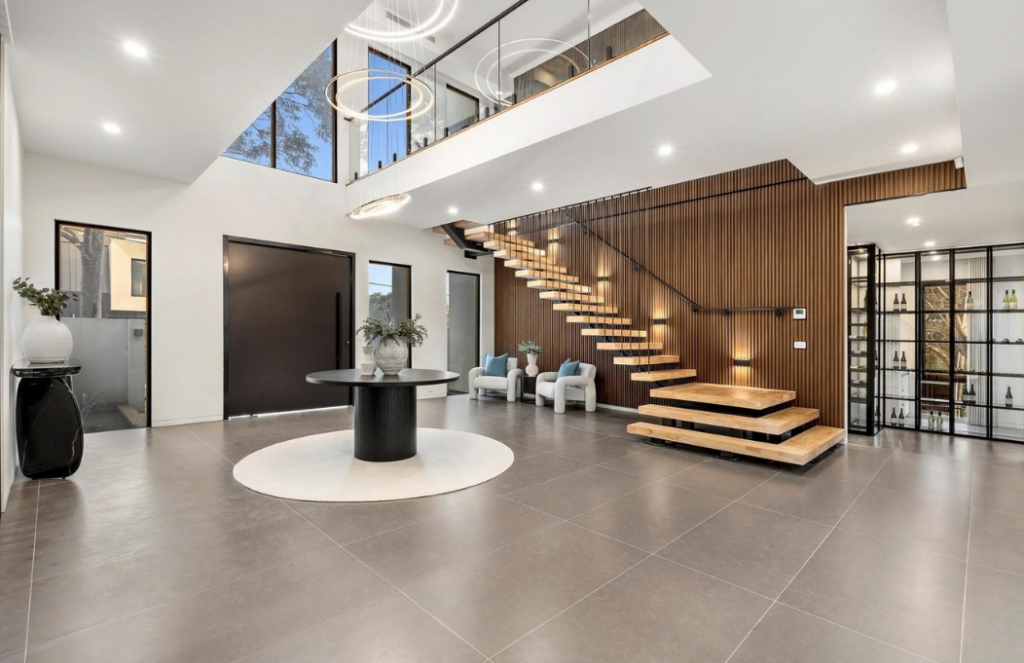 Grand entry with floating timber staircase, timber feature wall and sculptural furnishings in a luxury house in Doncaster.