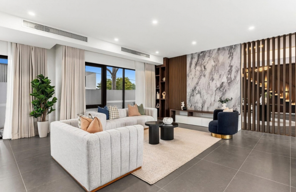 Neutral living room with curved sofas, navy accent chair and marble feature wall in a luxury house in Doncaster.