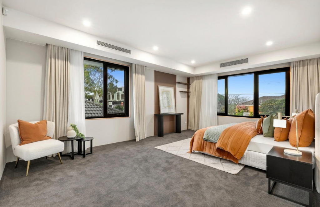 Spacious bedroom with orange bedding, neutral armchair and large windows in a luxury house in Doncaster.
