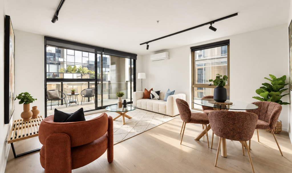 Professionally staged open-plan living and dining area with warm rust accents, neutral furniture and indoor greenery in an apartment in Collingwood.