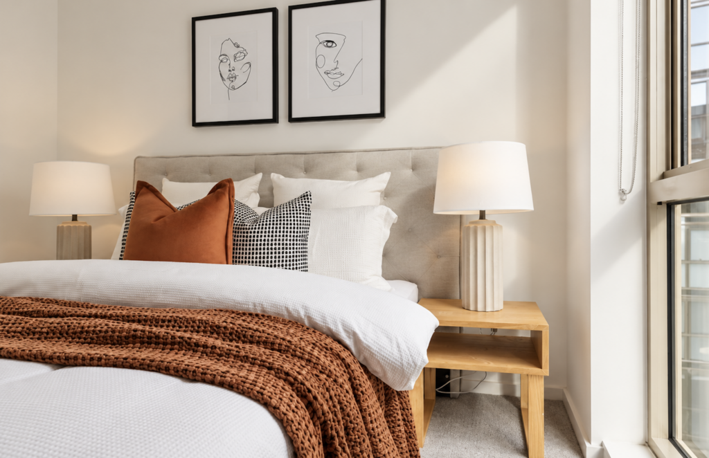Styled bedroom with neutral upholstered bedhead, layered white bedding, rust cushions and textured throw in an apartment in Collingwood.
