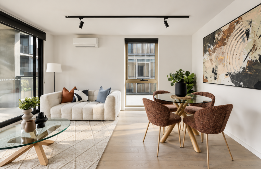 Professionally staged open-plan living and dining room with sculptural furniture, warm rust tones and contemporary artwork in an apartment in Collingwood.