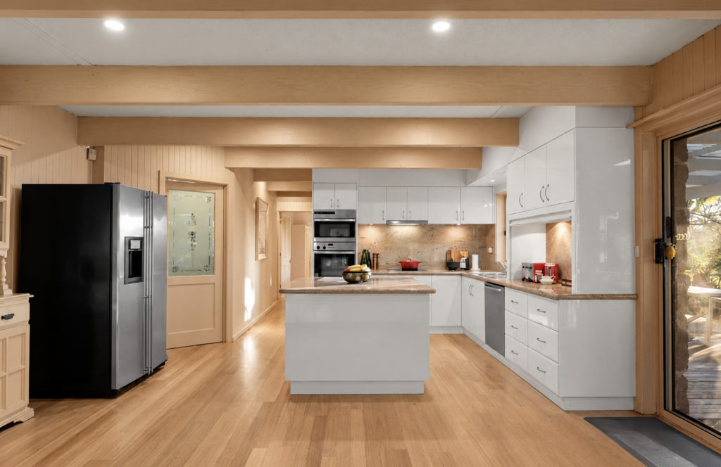 Spacious white kitchen with central island, timber flooring, exposed ceiling beams and warm natural light in a house in Cockatoo.