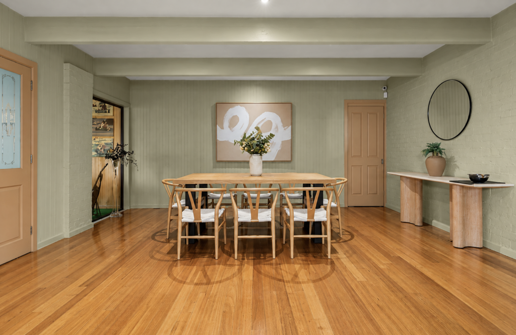 Dining room with timber table and wishbone chairs, abstract artwork, floral arrangement and soft green walls in a house in Cockatoo.