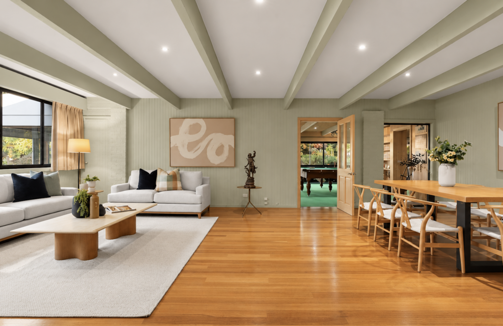 Open-plan living and dining area styled with neutral furniture, warm timber tones, abstract artwork and greenery in a house in Cockatoo.