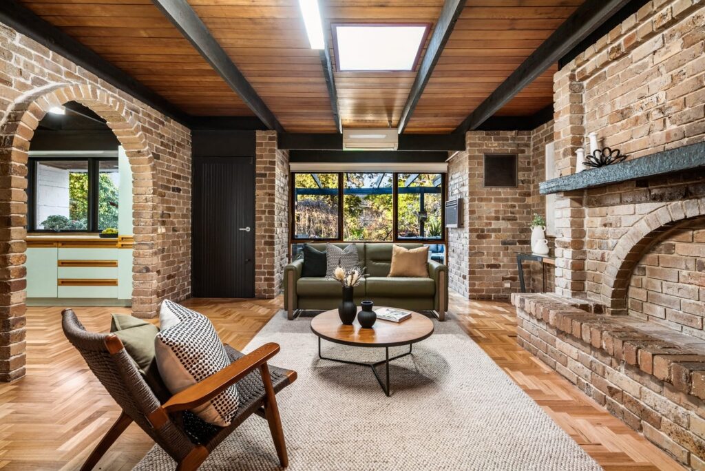 Warm living room styling with green sofa, timber coffee table, woven chair and exposed brick architectural features in a brick house in Vermont.